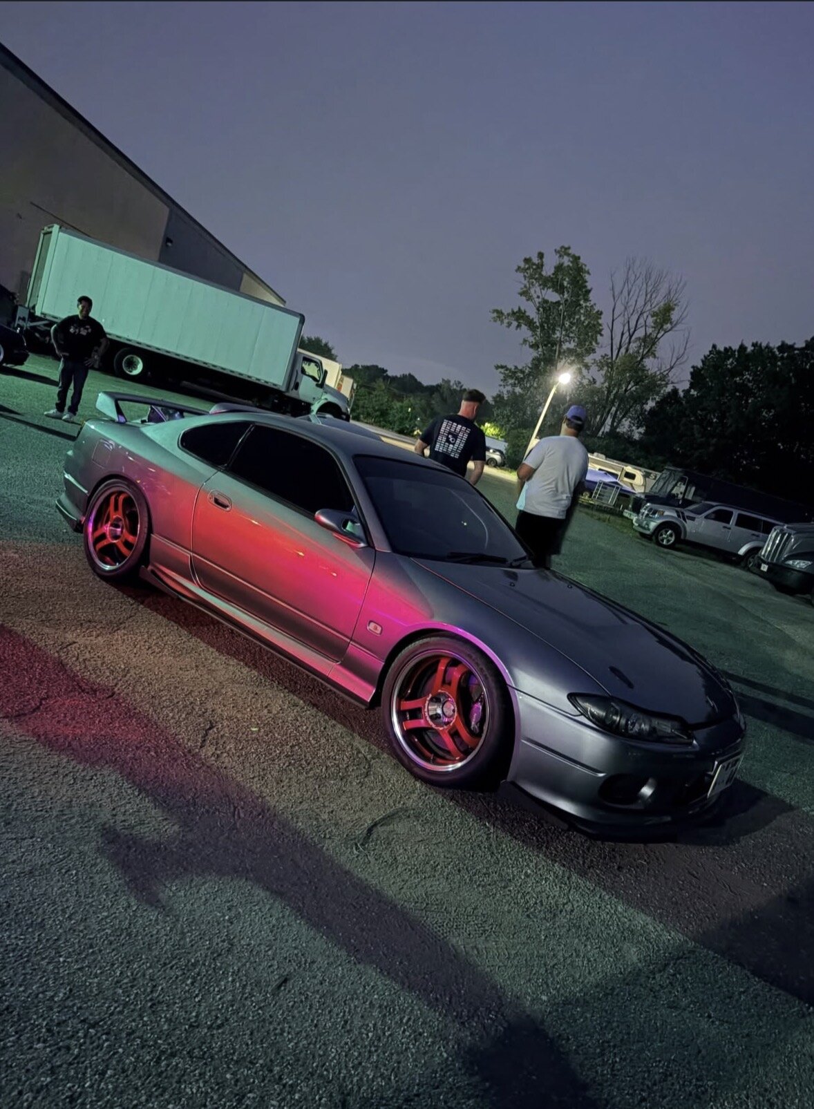 Silver Nissan Silvia S15 at night, three-quarter side view with red wheels